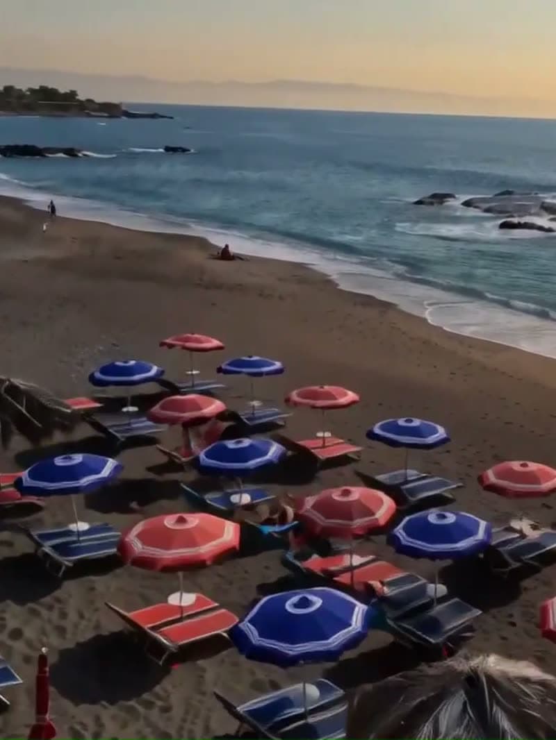 Gli ombrelloni blu e rossi aperti sulla sabbia scura del lido